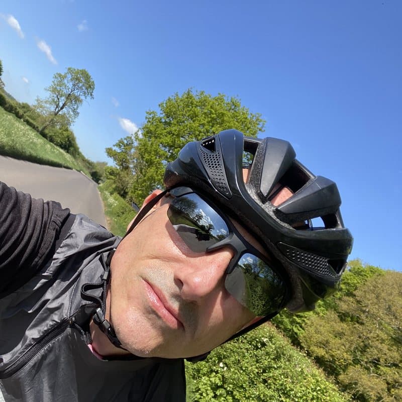 David Stimson in helmet and sunglasses on a sunlit country lane
