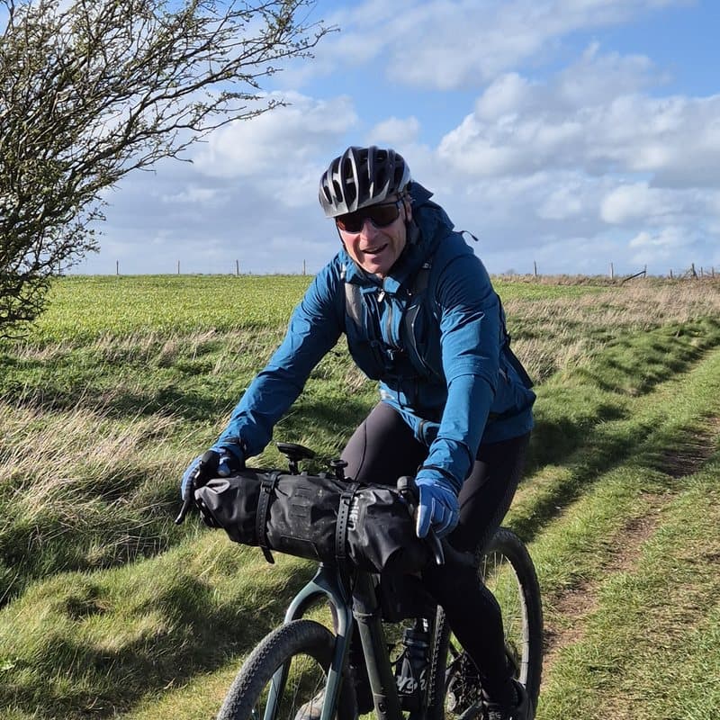 Jerry Gore riding a loaded gravel bike along a grass field track
